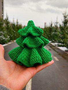 a hand holding a knitted christmas tree ornament in front of a road