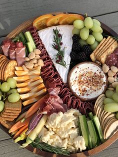 a wooden platter filled with cheese, crackers, grapes and other food items