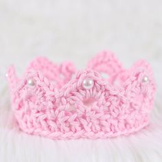 a pink crochet crown with pearls on it sitting on a white furnishing