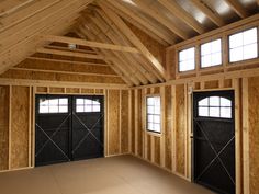 an empty room with two garage doors and windows in the wall, surrounded by wood framing