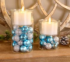 two glass vases filled with ornaments on top of a wooden table next to a candle