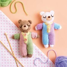 two knitted teddy bears sitting on top of a table next to yarn and knitting needles