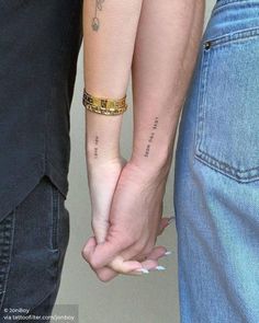 two people holding hands with tattoos on their arms and one has a gold chain around the wrist