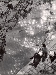 two people sitting on the edge of a body of water