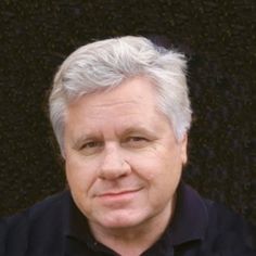 a man with grey hair and black shirt posing for a photo in front of a wall