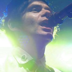 a man singing into a microphone while wearing a white shirt and tie with green lights behind him