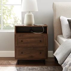 a nightstand with a lamp on top of it next to a bed in a bedroom