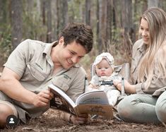 a man and woman sitting on the ground reading a book to a baby