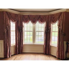 an empty room with large windows and drapes on the window sill, along with wooden flooring