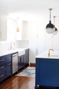 a kitchen with white cabinets and blue island in front of the sink is lit by two pendant lights