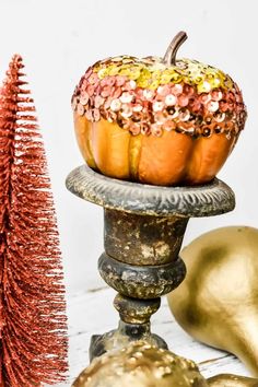 an orange pumpkin sitting on top of a metal stand next to a small christmas tree