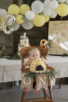 a baby sitting in a wooden chair with balloons and decorations around him on the table