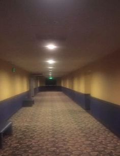 an empty hallway with benches and lights on either side of the corridor is lit by recessed lighting