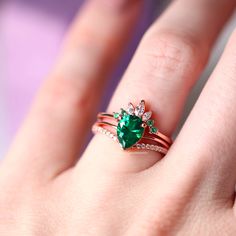 a woman's hand with two rings and a green heart shaped ring on it