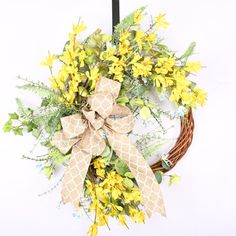 a wreath with yellow flowers hanging on a wall next to a black hook and white background