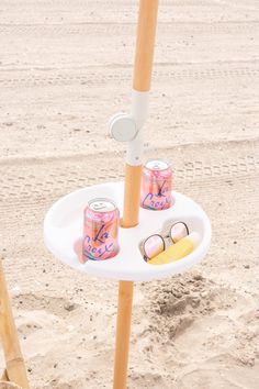 a table with two cans and sunglasses on it, in the sand at the beach