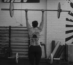 a woman lifting a barbell in a crossfit gym with her back to the camera