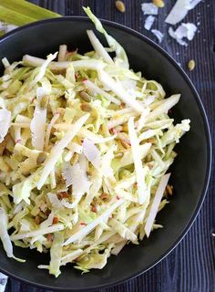 a black bowl filled with coleslaw on top of a wooden table next to celery sticks