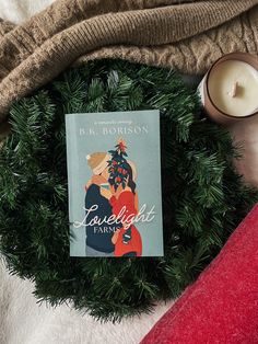 a book sitting on top of a blanket next to a candle and some christmas decorations