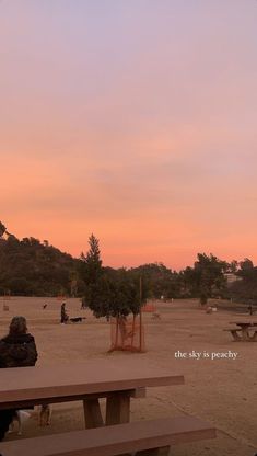 a person sitting at a picnic table watching the sun go down in an empty park