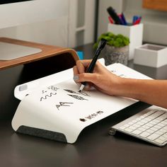 a person writing on a piece of paper next to a keyboard and computer monitor,