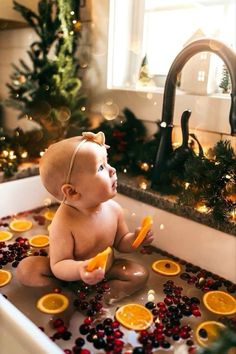 a baby sitting in a bathtub with orange slices and cranberries on the floor