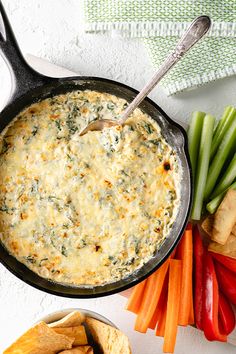 a skillet filled with dip surrounded by veggies and crackers on the side