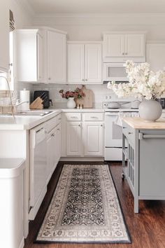 a kitchen with white cabinets and wood flooring has a rug on the floor in front of the stove