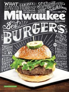 a hamburger with lettuce and pickles on it in front of a chalkboard