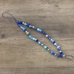 a long beaded necklace with blue and gold beads on a wooden table next to a pair of scissors