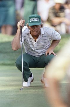 a man kneeling down on top of a green golf field holding a putter's club