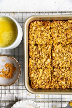 a baking dish with granola next to two bowls of orange juice and a spoon