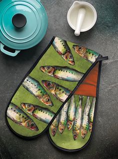 two oven mitts with fish on them next to a pot holder and coffee mug