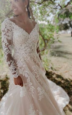 a woman in a wedding dress standing under a tree with her hand on her hip