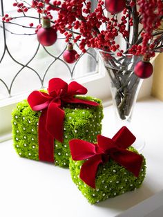 two green boxes covered in moss with red bows and balls on top, sitting next to each other