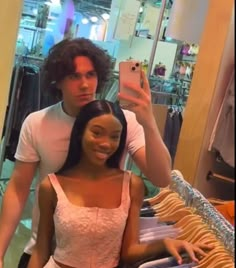 a man taking a selfie with a woman in front of a clothing store mirror