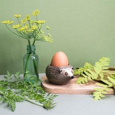 a hedgehog egg sitting on top of a wooden board next to flowers and greenery