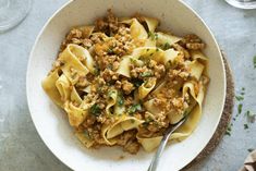 a white bowl filled with pasta and meat on top of a table next to wine glasses