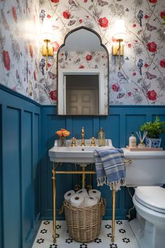 a bathroom with blue walls and floral wallpaper, gold fixtures and a white toilet