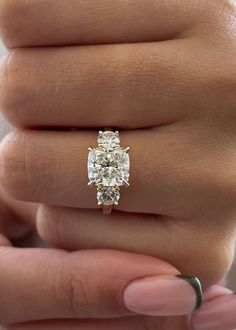 a woman's hand holding an engagement ring with three stones on the band and one stone