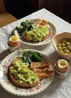 two plates filled with food sitting on top of a white table cloth next to bowls of eggs