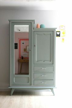 an armoire with two drawers and a mirror on the front, against a white wall