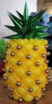 a large yellow pineapple balloon sitting on top of a wooden table next to balloons