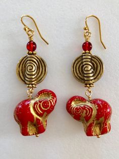 "Beautiful scarlet red Czech glass elephants with gold wash wire wrapped with 5/8\" solid brass spiral coin bead and topped with transparent red and metallic gold Czech glass beads. Premium Czech glass elephants are 20 x 23mm 3D glass beads. Coin element is two-sided and accented with antique gold plated pewter daisies. Earrings hang from 14k gold plated French ear hooks. Total drop is 2 1/4\"." Handmade Eclectic Red Jewelry, Adjustable Eclectic Red Jewelry, Adjustable Red Spiral Jewelry, Red Brass Wire Wrapped Jewelry, Red Wire Wrapped Brass Jewelry, Red Elephant, Red Sea Glass, Elephant Earrings, Sea Glass Earrings