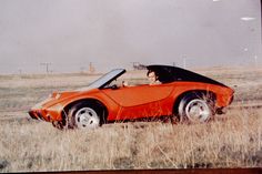 an orange sports car is parked in the middle of a field with its hood up