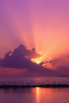 the sun is setting over the ocean with clouds in the sky and water below it