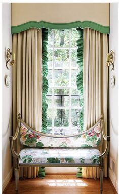 a bench sitting in front of a window next to a curtained window with green leaves on it