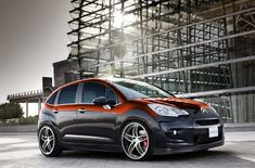 an orange and black car is parked in front of a building with scaffolding