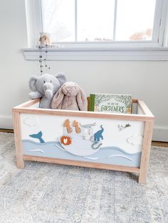 a toy chest with stuffed animals and books in it sitting on the floor next to a window