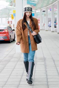 a woman walking down the street wearing boots and a hat on top of her head